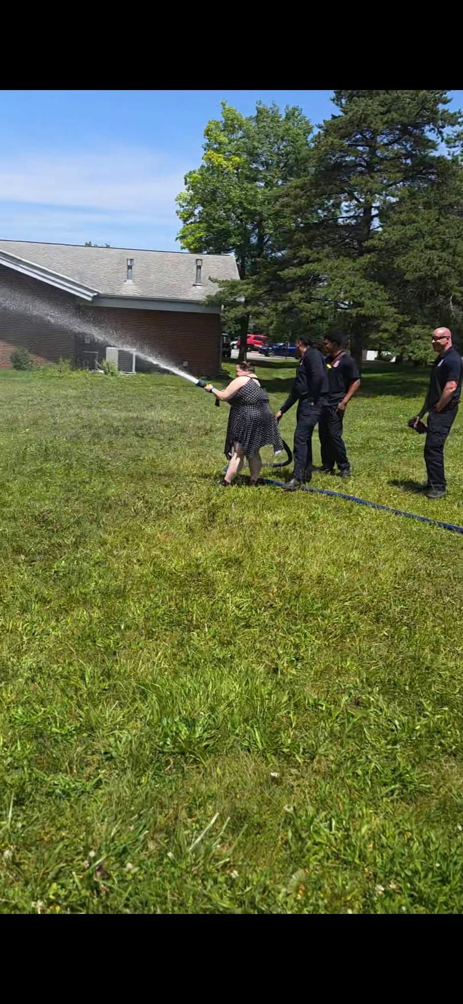 Forest Park firefighters helping an adult try a fire hose outdoors