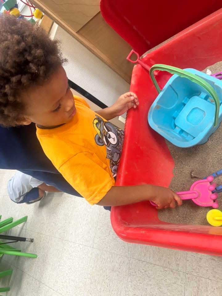 A child explores a sensory bin with scoops and toys.