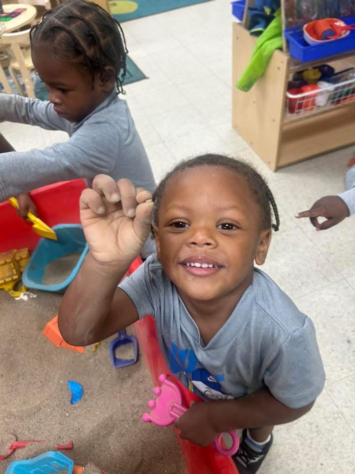A smiling child plays at a classroom sensory table.