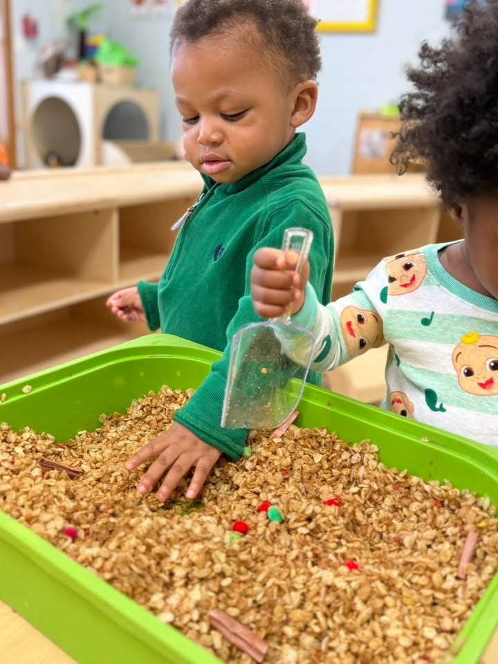 A toddler explores a tray of sensory materials.