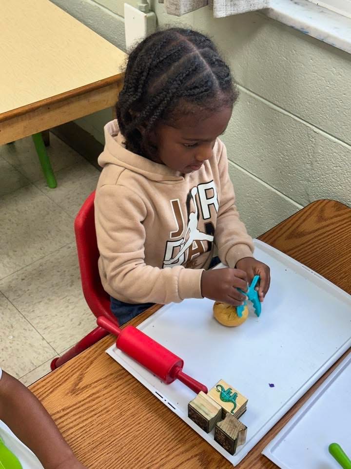 A child explores play dough with classroom tools at a table.
