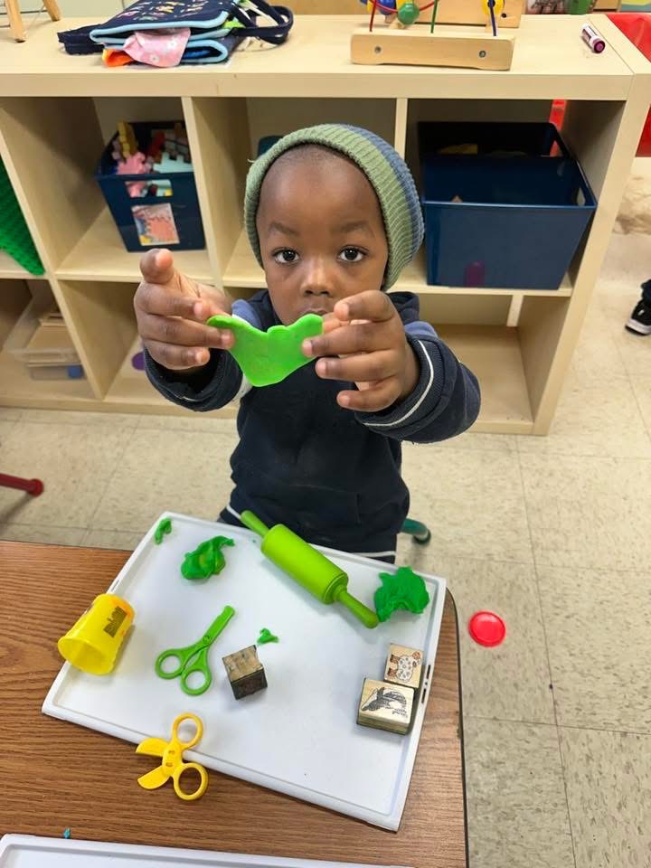 A child shows a green play dough creation during table play.