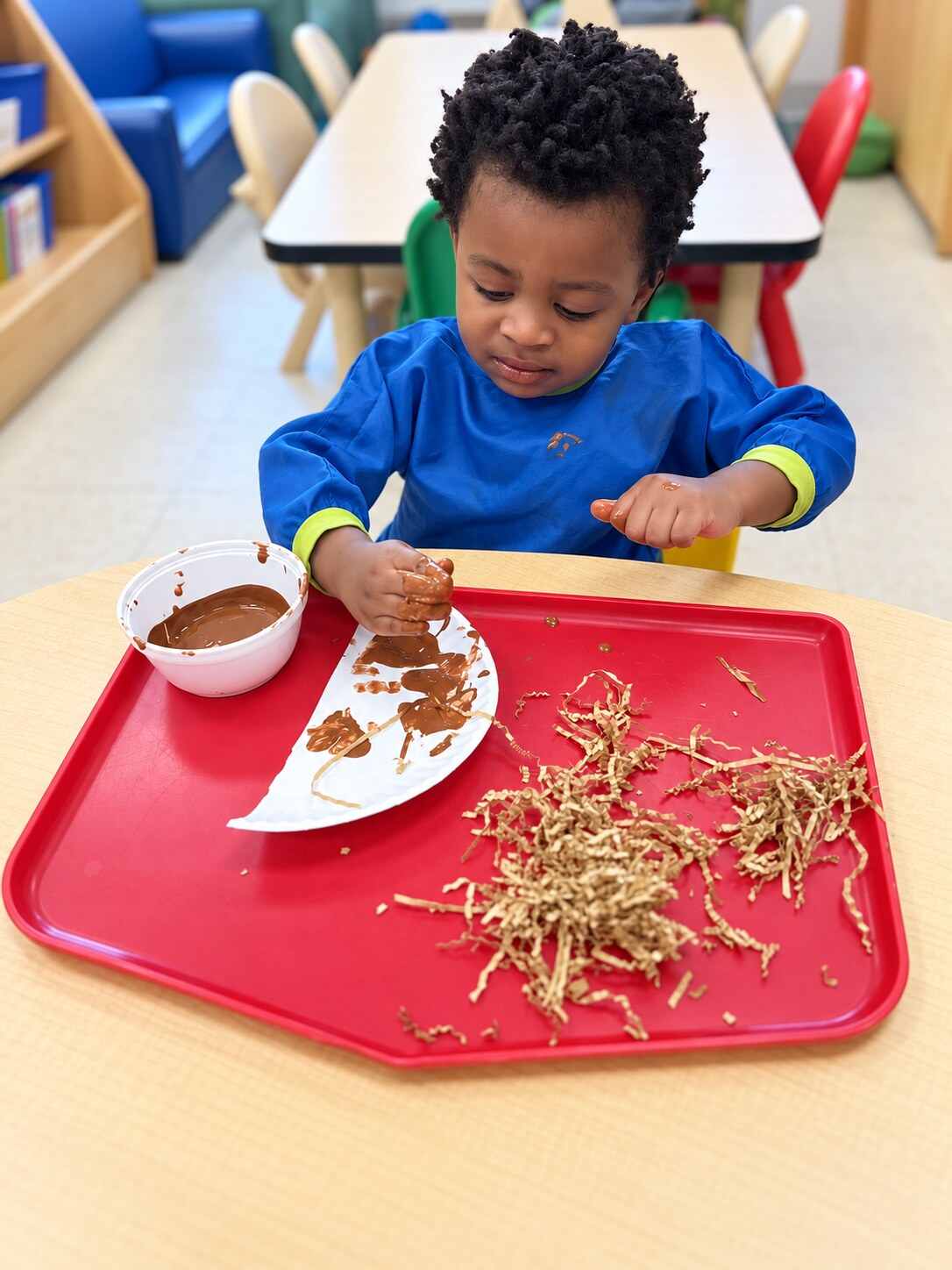 A toddler explores a tub of natural materials.