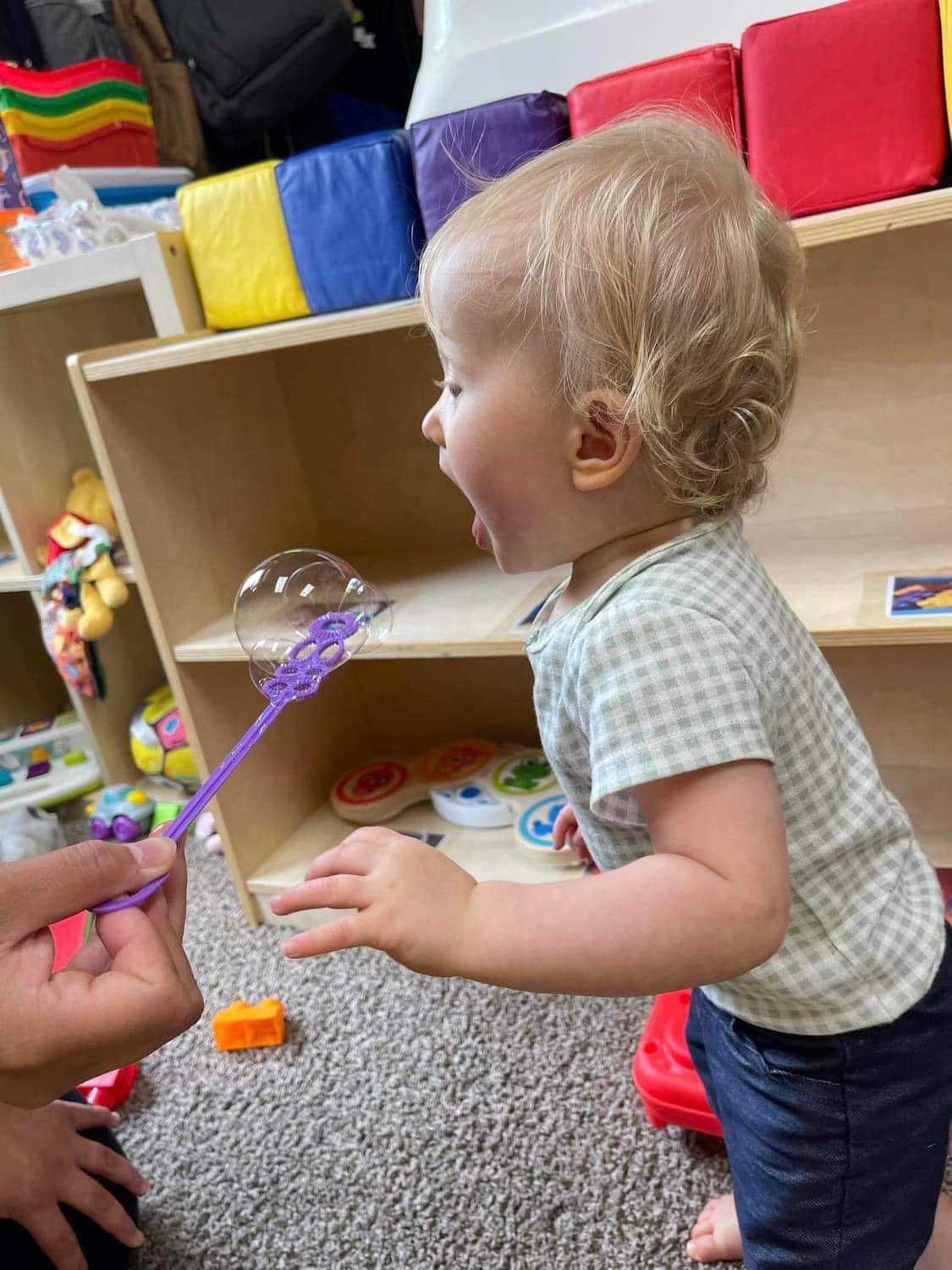 A toddler watches and reaches toward bubbles during play.