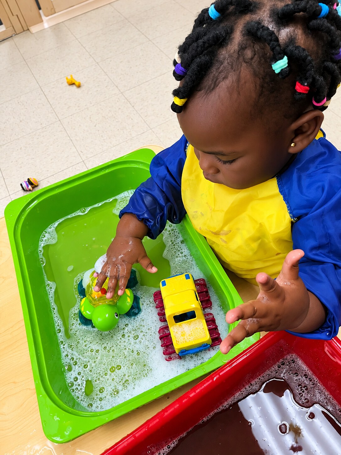 A toddler explores materials in a green sensory bin.