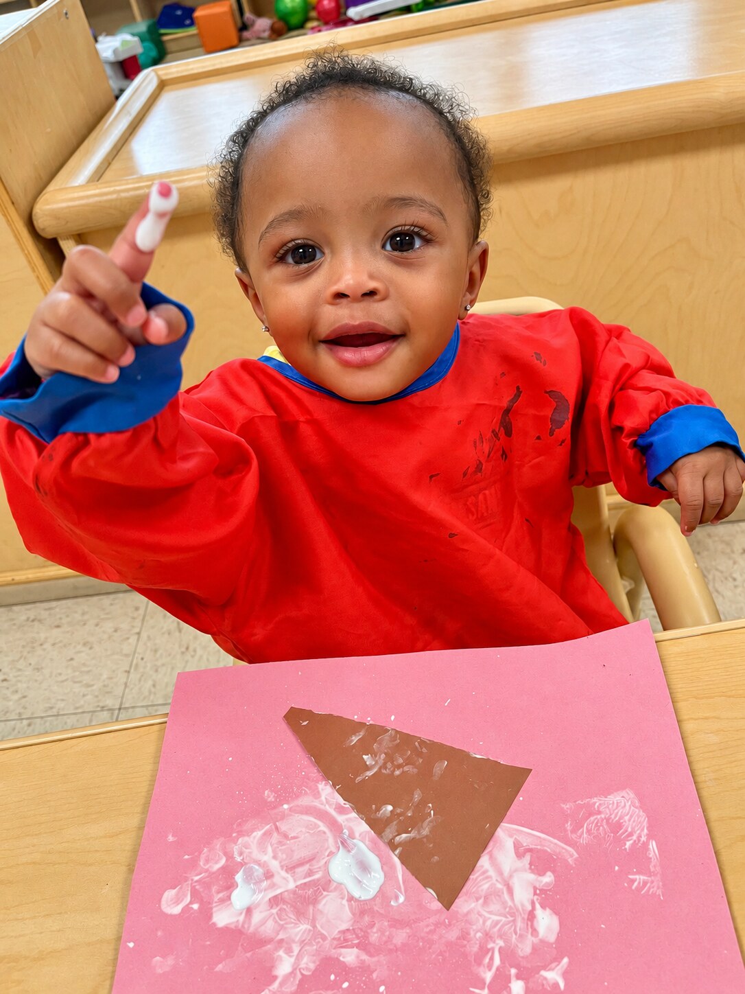 A toddler smiles while holding a classroom object.