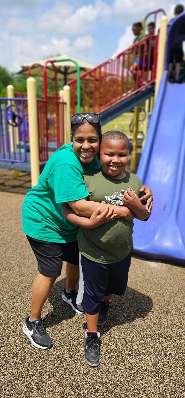 A teacher and child share a happy moment outside.