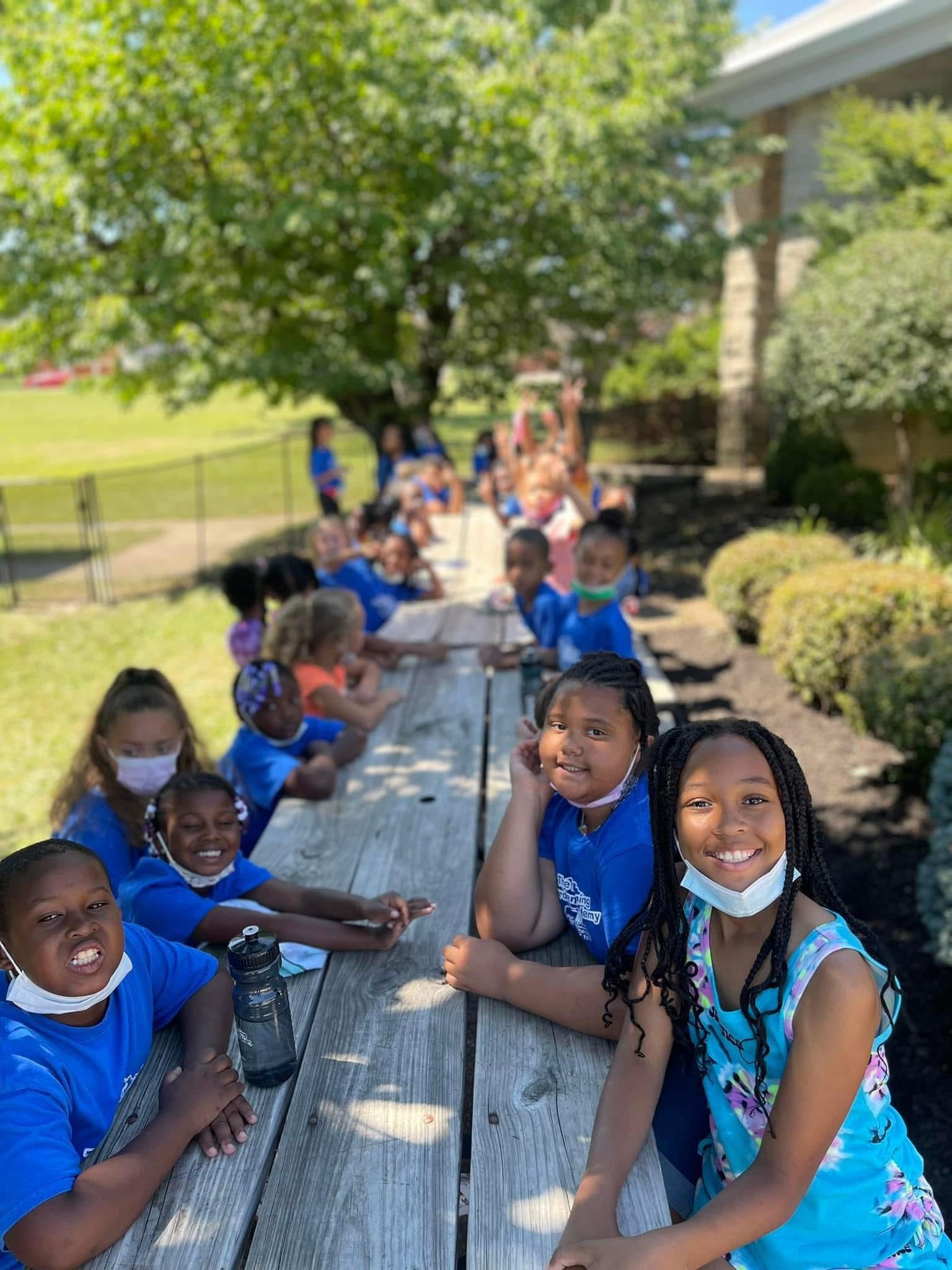 Friends share an outdoor picnic beneath a tree.