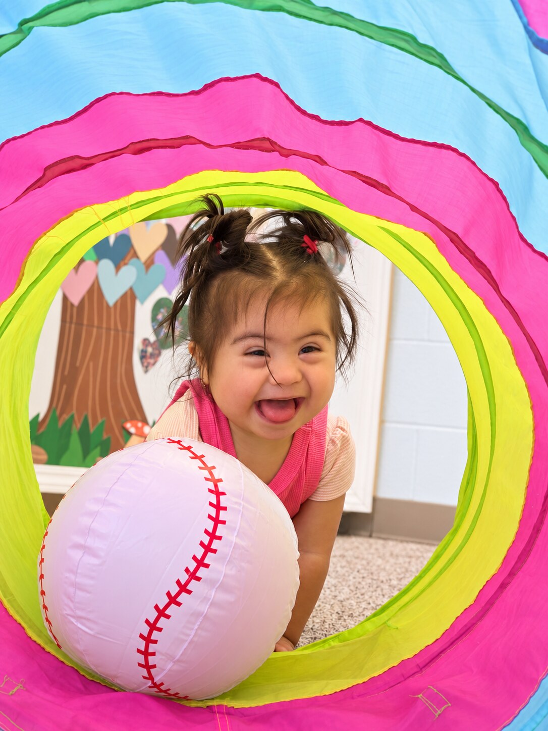 A toddler plays with a ball and fabric tunnel.